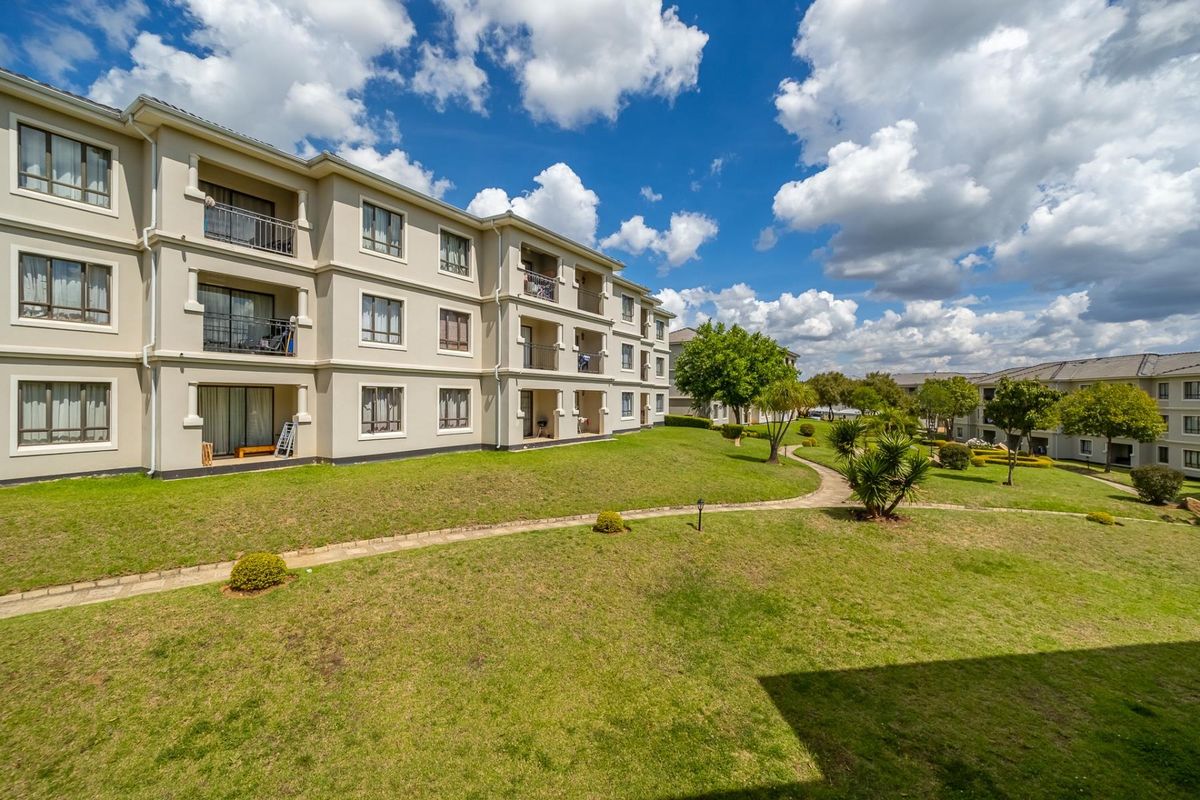 A view of the apartment complex rear elevation featuring multiple balconies, sliding glass doors, and well-maintained communal garden areas with paved walkways.