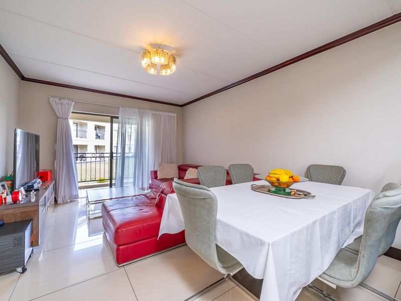 Bright open-plan living and dining area featuring large format floor tiles, crown molding, and a sliding glass door leading to a private balcony.