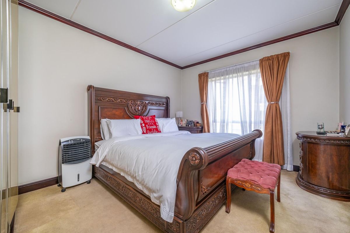 A spacious bedroom featuring neutral walls, crown molding, and a large window with natural light, providing a comfortable and functional living space.