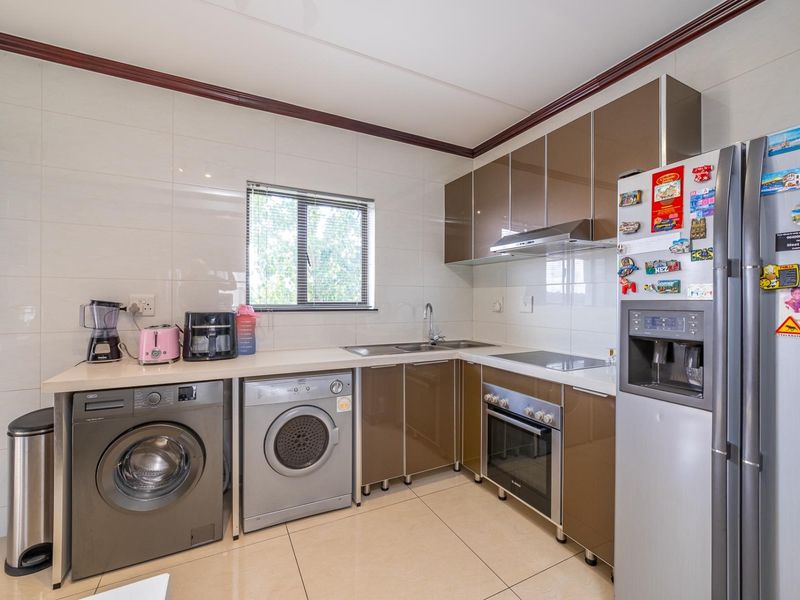 A functional kitchen featuring modern brown cabinetry, integrated oven and hob, stainless steel sink, and tiled finishes throughout.