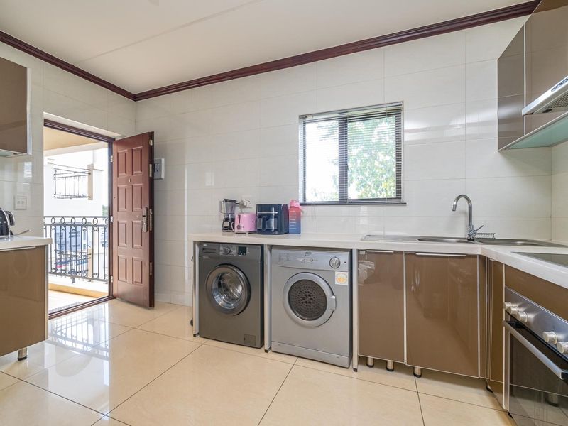 Modern kitchen featuring high-gloss cabinetry, built-in oven, extractor fan, and integrated laundry appliances, with direct access to a private balcony.