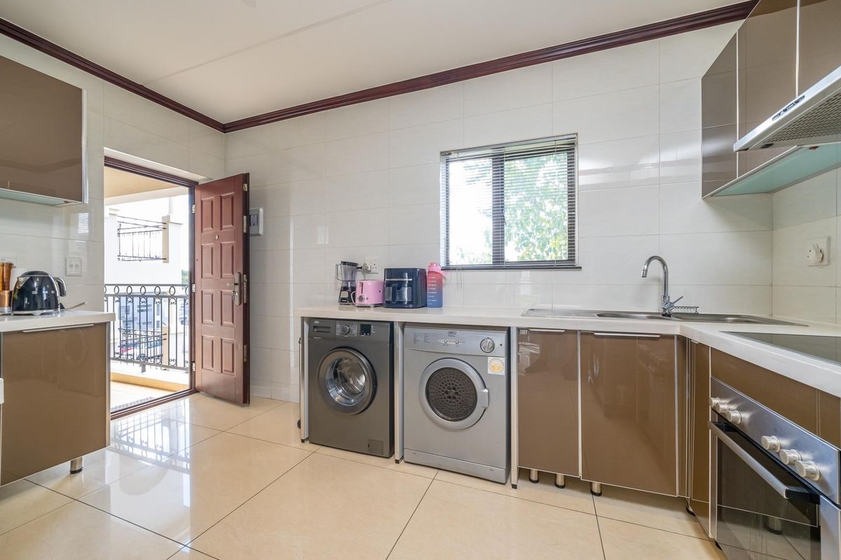 Modern kitchen featuring high-gloss cabinetry, built-in oven, extractor fan, and integrated laundry appliances, with direct access to a private balcony.