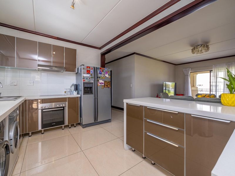 Modern open-plan kitchen featuring high-gloss cabinetry, stone countertops, and integrated appliances, seamlessly flowing into the adjacent living area.