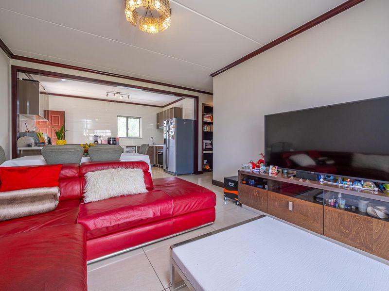 Open-plan living area featuring tiled floors and a connected kitchen space with built-in cabinetry, providing a functional and integrated layout.