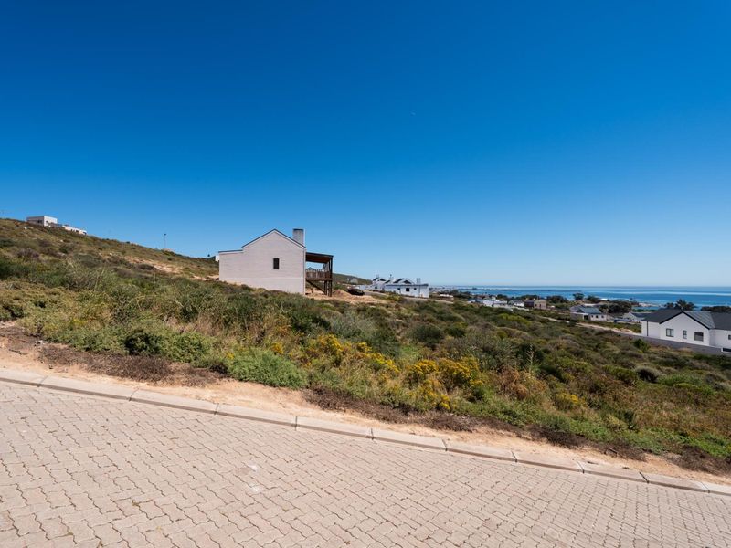 A scenic view of the coastal landscape and surrounding residential properties from an elevated paved street position.