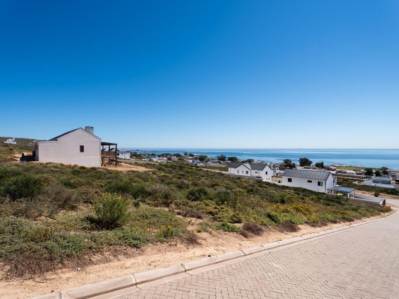 A scenic elevated view of the coastal residential area and ocean from a paved street.