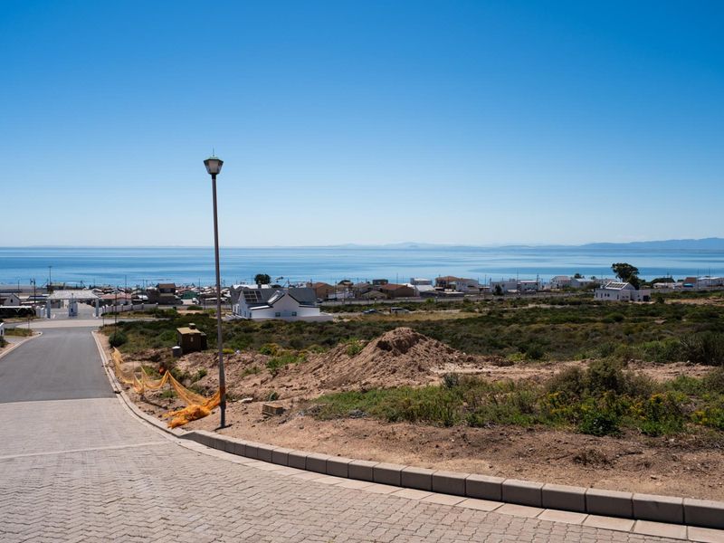 A scenic view overlooking a coastal residential area with a paved driveway and street infrastructure in the foreground.