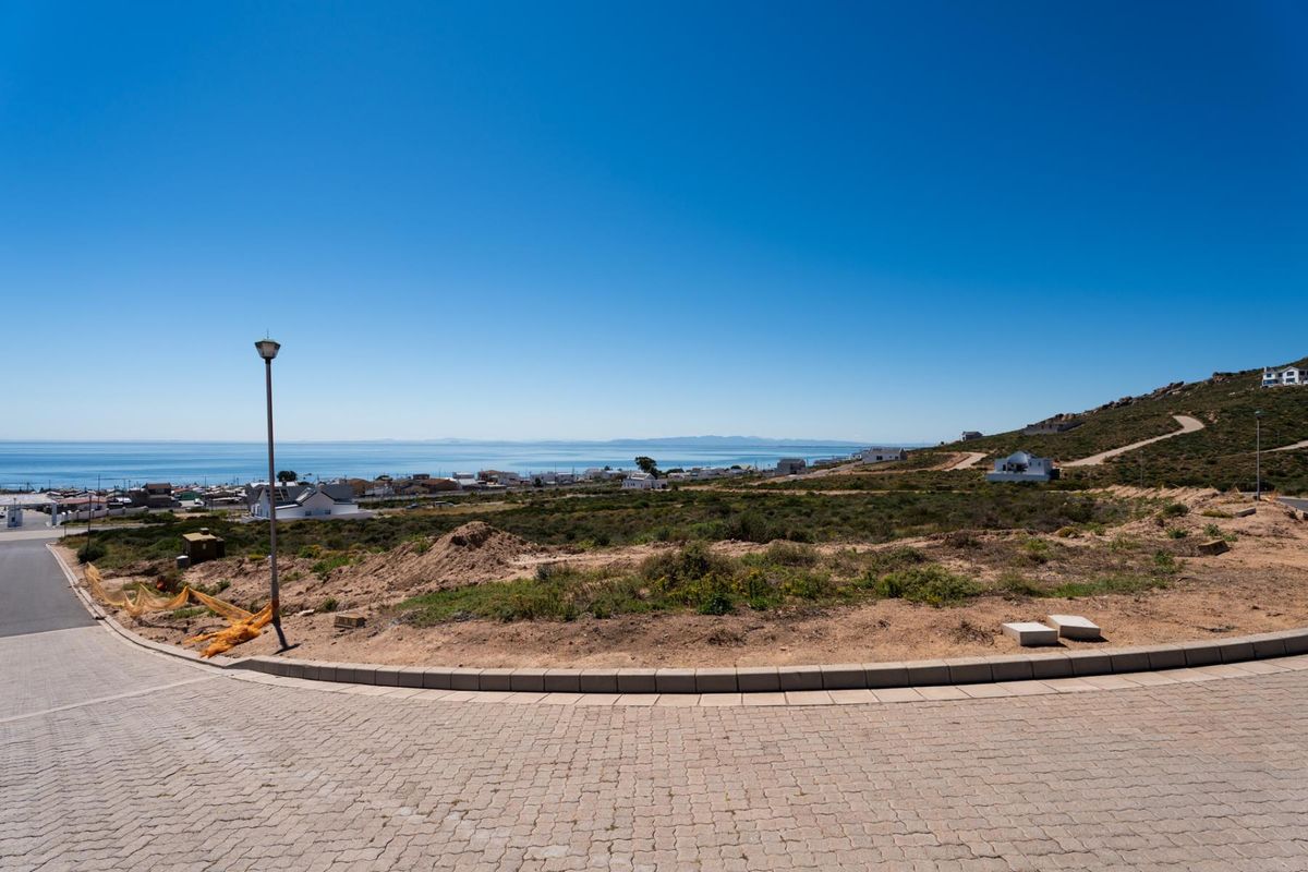 A scenic view overlooking a coastal residential area from a paved street, showcasing the surrounding landscape and ocean horizon.