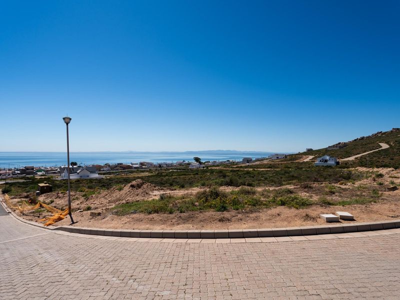 A scenic view overlooking a coastal residential area from a paved street, showcasing the surrounding landscape and ocean horizon.