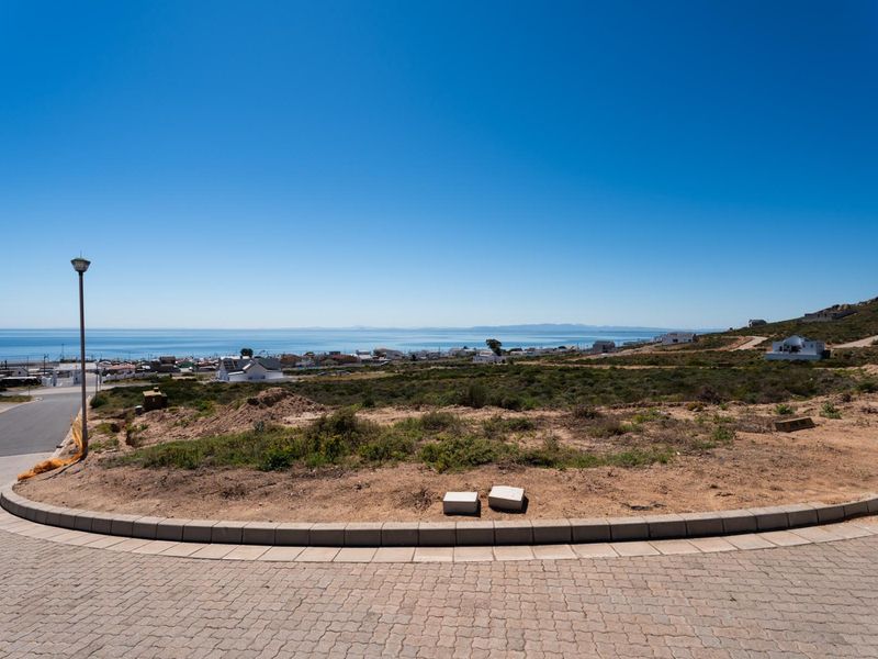 A vacant residential plot featuring a paved driveway, concrete curbing, and expansive coastal views over the surrounding neighborhood.