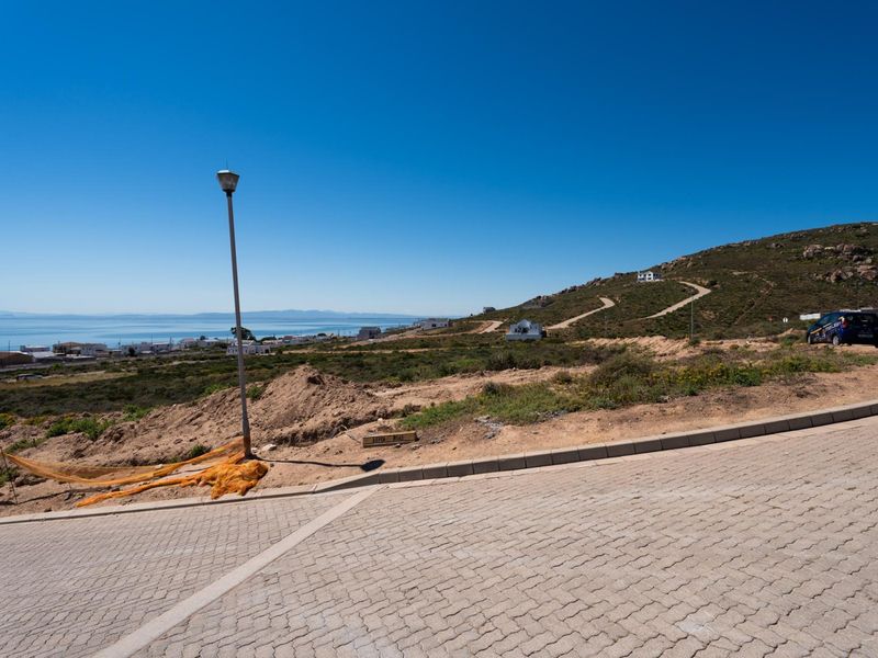 A view of a vacant residential plot featuring a paved driveway, street lighting, and coastal landscape views.