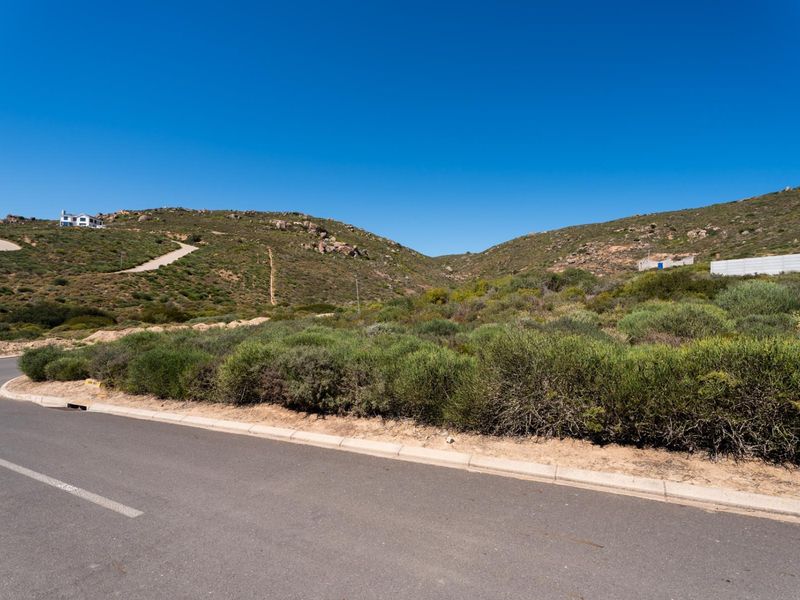 A view of the paved street and concrete curbing bordering the vacant residential land, featuring natural hillside terrain and surrounding landscape.