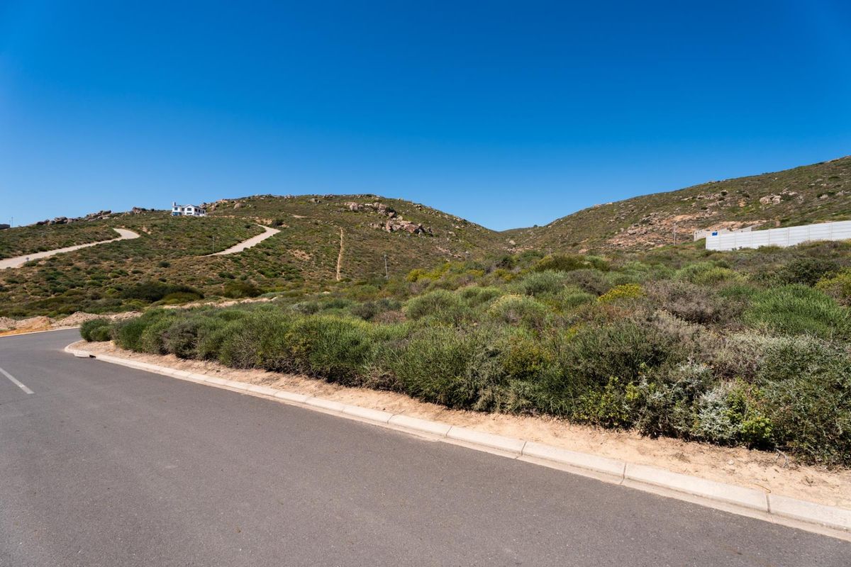 A view of the paved street and concrete curbing bordering the vacant residential land, set against a natural hilly landscape.