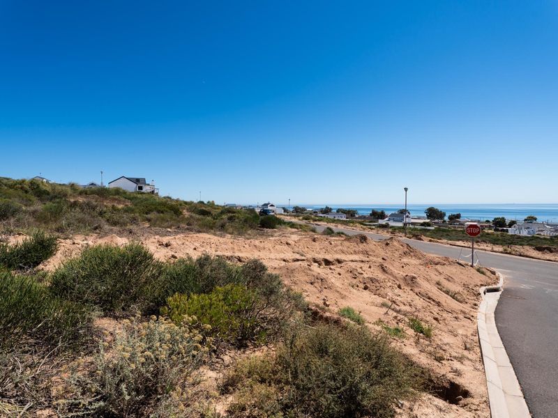 A vacant residential plot situated on a hillside, featuring coastal views and direct access to a paved street with established curbing.