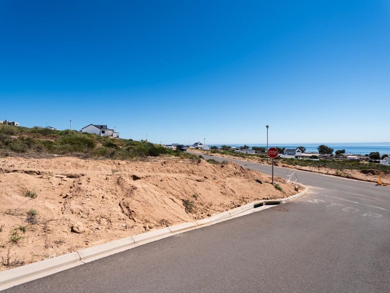 A street-level view of the vacant residential land, featuring paved road access, concrete curbing, and coastal views in the distance.