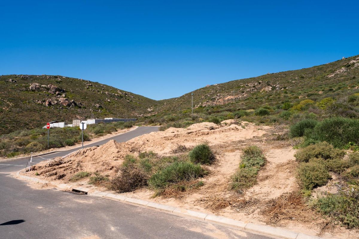 A vacant residential plot situated on a paved road with established concrete curbing and natural hillside surroundings.