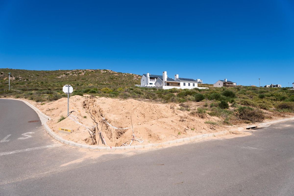 A vacant residential plot featuring an open utility trench and exposed cabling at the street corner, situated in a coastal development.
