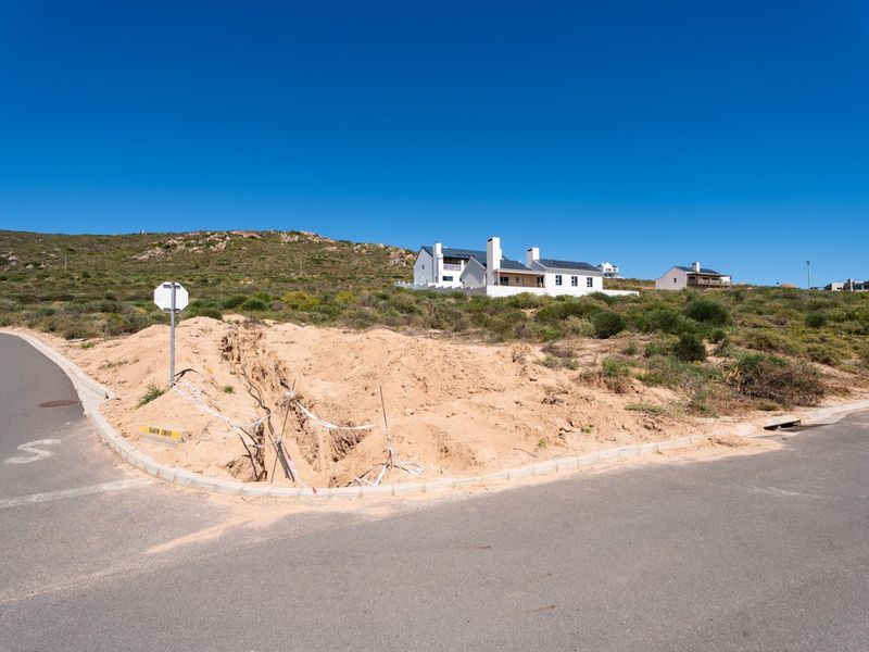 A vacant residential plot featuring an open utility trench and exposed cabling at the street corner, situated in a coastal development.