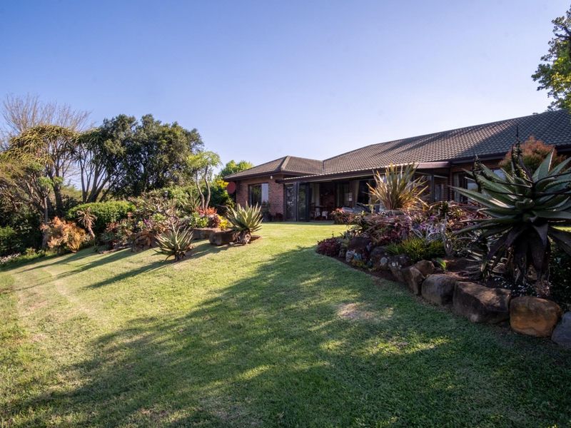 A well-maintained rear exterior view of the house featuring a landscaped garden, stone retaining walls, and a tiled roof with sliding door access.