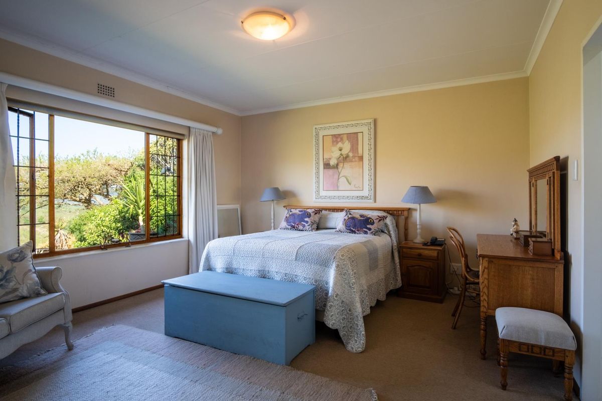 A well-lit bedroom featuring carpeted flooring and a large window with garden views, offering a comfortable and functional living space.