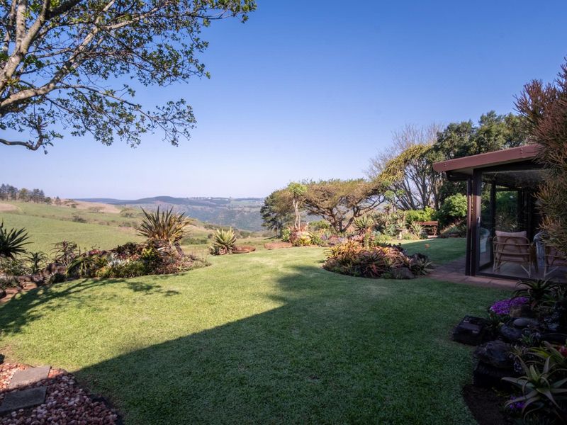 A beautifully landscaped garden featuring a lush lawn, rockery beds, and expansive views of the surrounding countryside, adjacent to a glass-enclosed patio area.