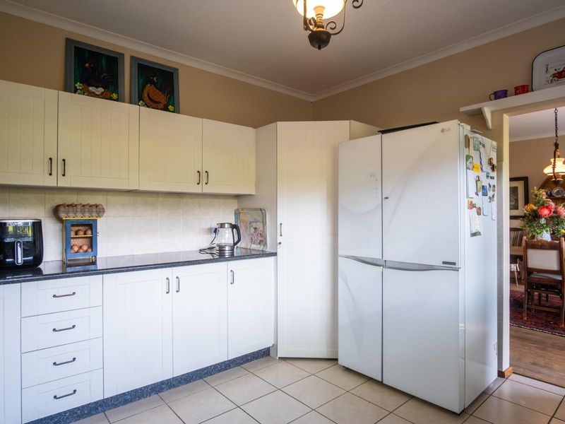 A functional kitchen featuring white shaker-style cabinetry, dark granite countertops, tiled backsplash, and ceramic flooring, with a convenient corner pantry cupboard.