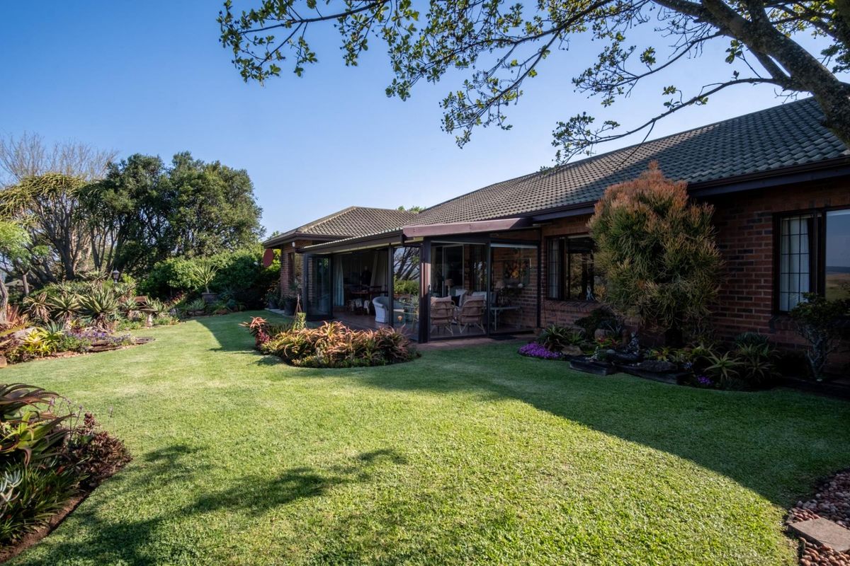Rear view of a brick house featuring a well-maintained garden, lawn, and an enclosed patio area with sliding glass doors.
