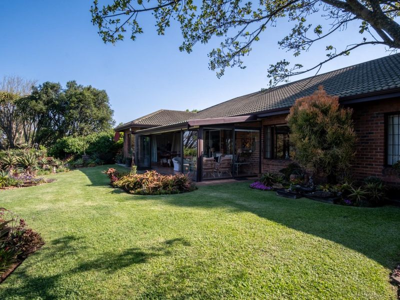 Rear view of a brick house featuring a well-maintained garden, lawn, and an enclosed patio area with sliding glass doors.