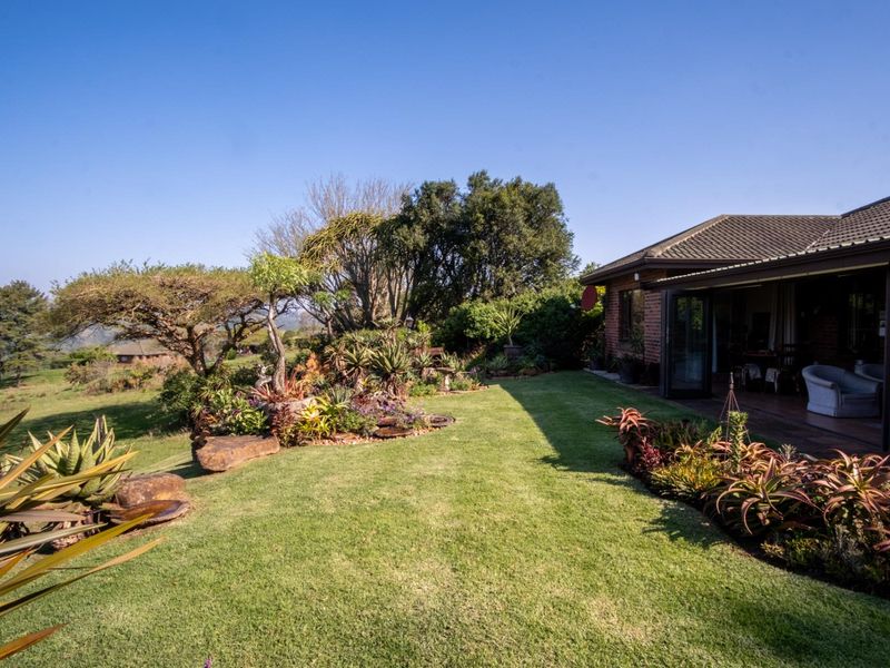 A well-maintained rear garden featuring established landscaping, a manicured lawn, and a covered patio area with sliding glass doors leading into the home.