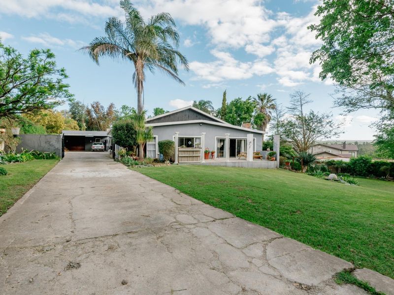 Front view of the property featuring a large concrete driveway, a covered patio area, and a spacious landscaped garden with a detached garage.