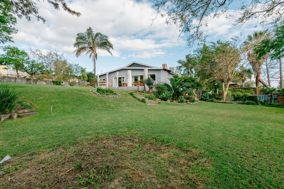 A spacious rear garden featuring a large lawn, mature landscaping, and stone steps leading up to the rear elevation of the house.