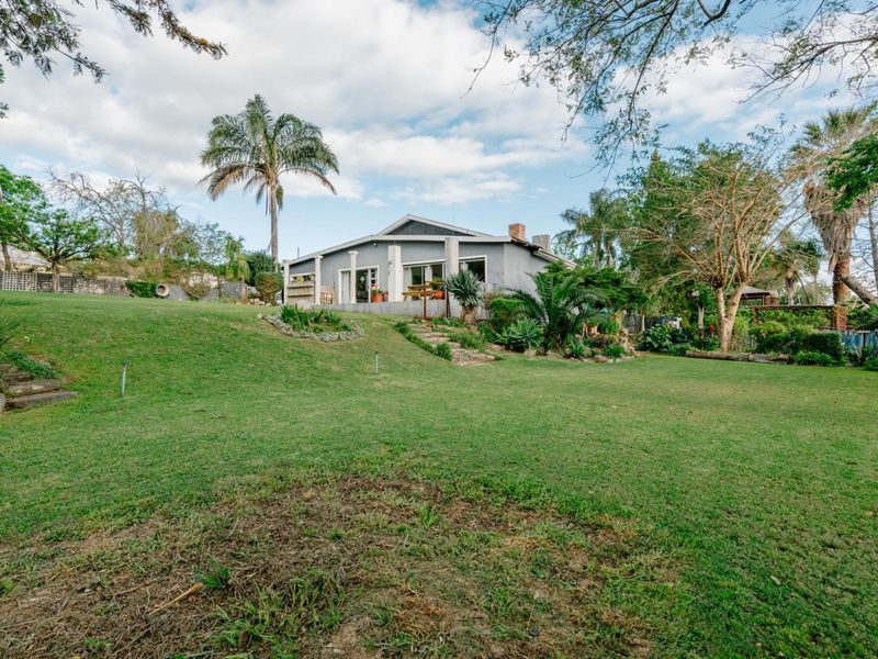 A spacious rear garden featuring a large lawn, mature landscaping, and stone steps leading up to the rear elevation of the house.