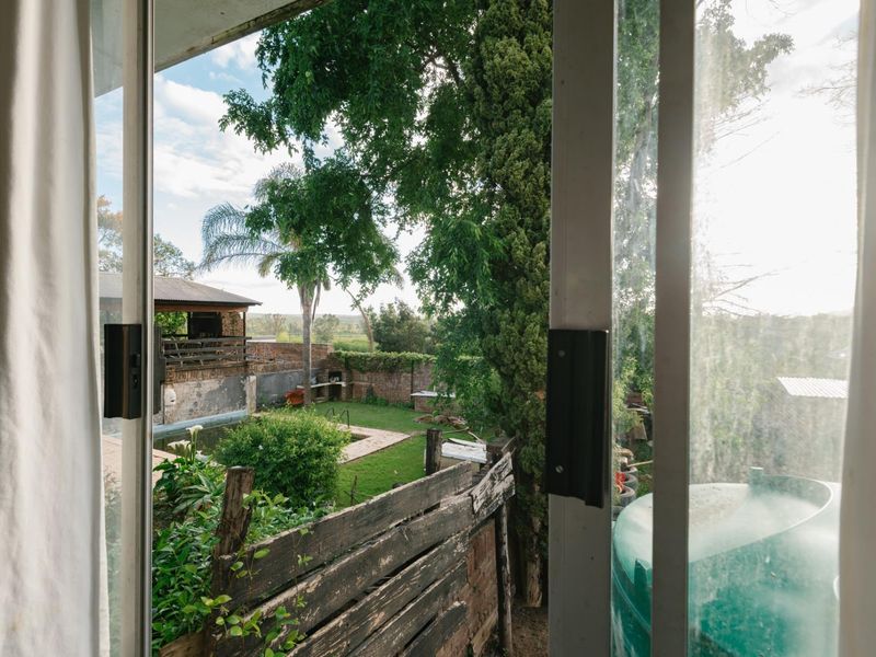 View from an interior doorway looking out onto a rear garden featuring a swimming pool, outdoor lapa, and established trees.