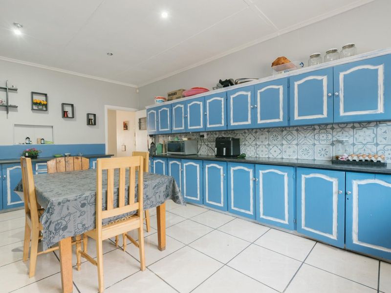 A spacious kitchen featuring extensive blue cabinetry, patterned tile backsplash, and light-colored floor tiles, offering a functional layout with ample storage space.