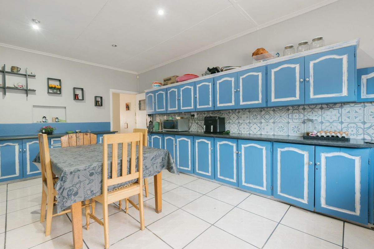 A spacious kitchen featuring extensive blue cabinetry, patterned tile backsplash, and light-colored floor tiles, offering a functional layout with ample storage space.