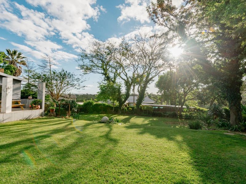 A spacious, well-maintained garden featuring a lush green lawn, mature trees, and an adjoining concrete patio area.