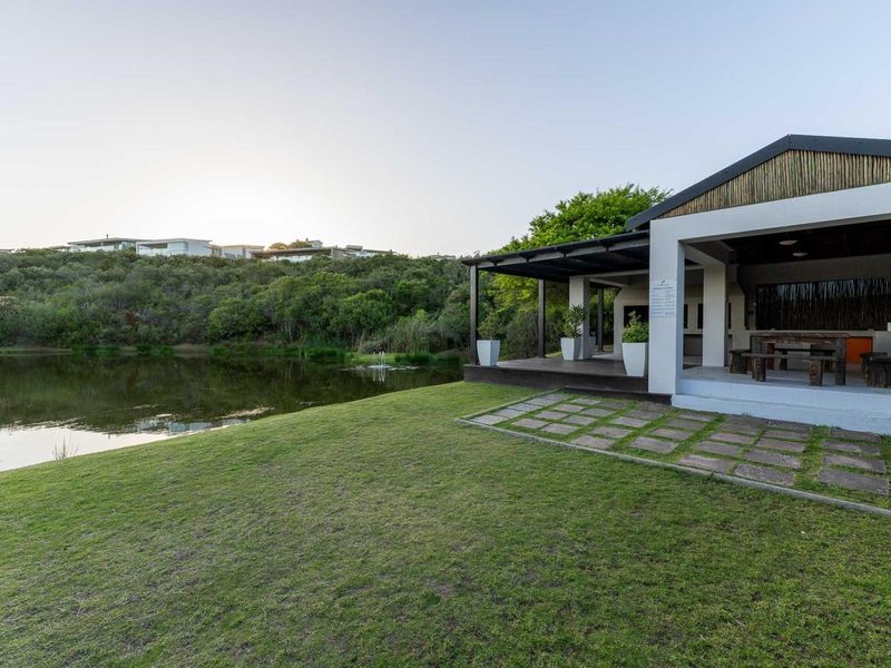 A spacious covered patio overlooking a tranquil pond and landscaped garden, featuring a built-in braai area perfect for outdoor entertaining.
