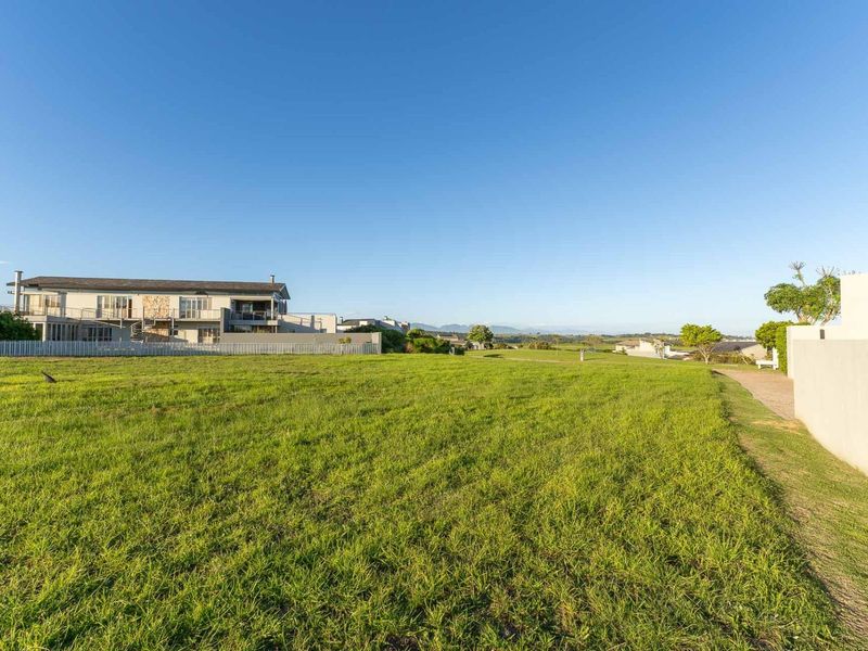 A wide-angle view of the property grounds featuring a large grass lawn, boundary wall, and paved driveway with surrounding estate views.