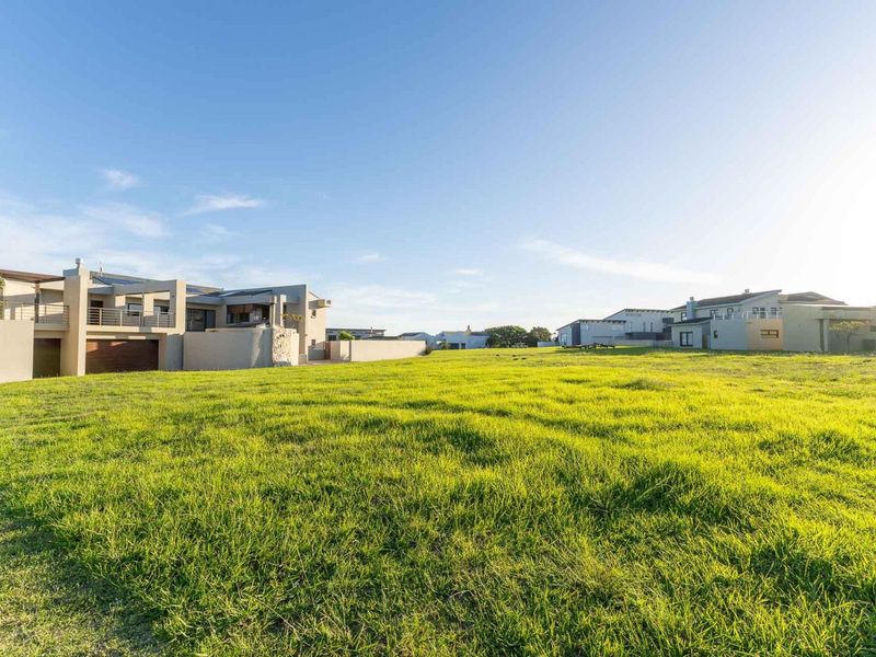A wide-angle view of a large, open grass lawn area adjacent to a modern multi-level residential property in a suburban estate setting.