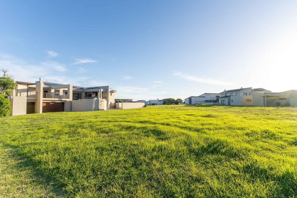 A wide-angle view of a large, open grass lawn area adjacent to a modern multi-level residential property in a suburban estate setting.