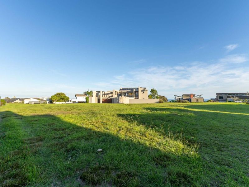 A wide-angle view of the rear exterior of a modern residential property featuring a large open lawn and boundary wall.