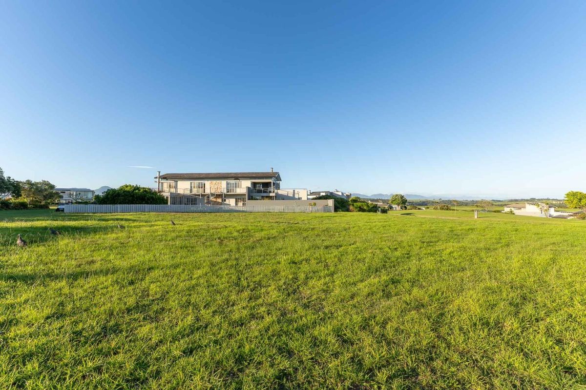 A wide-angle view of the rear elevation of a multi-level residential property set within a large, open grassy landscape.