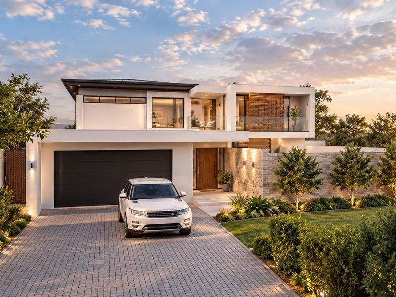 Modern luxury double-story residence featuring stone cladding, a paved driveway, double garage, and an upper-level balcony with glass balustrades.