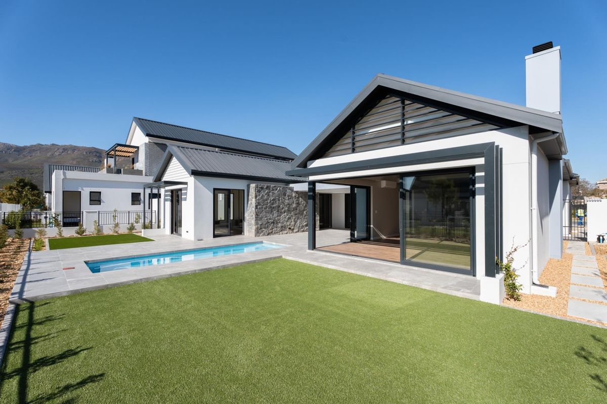 Modern rear exterior featuring a swimming pool, artificial lawn, stone feature wall, and large sliding glass doors leading to a covered patio area.