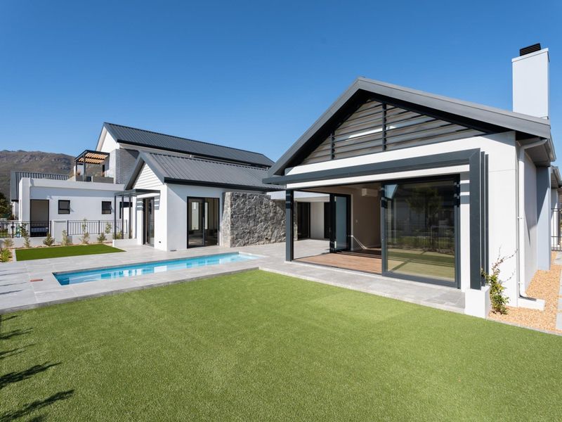 Modern rear exterior featuring a swimming pool, artificial lawn, stone feature wall, and large sliding glass doors leading to a covered patio area.