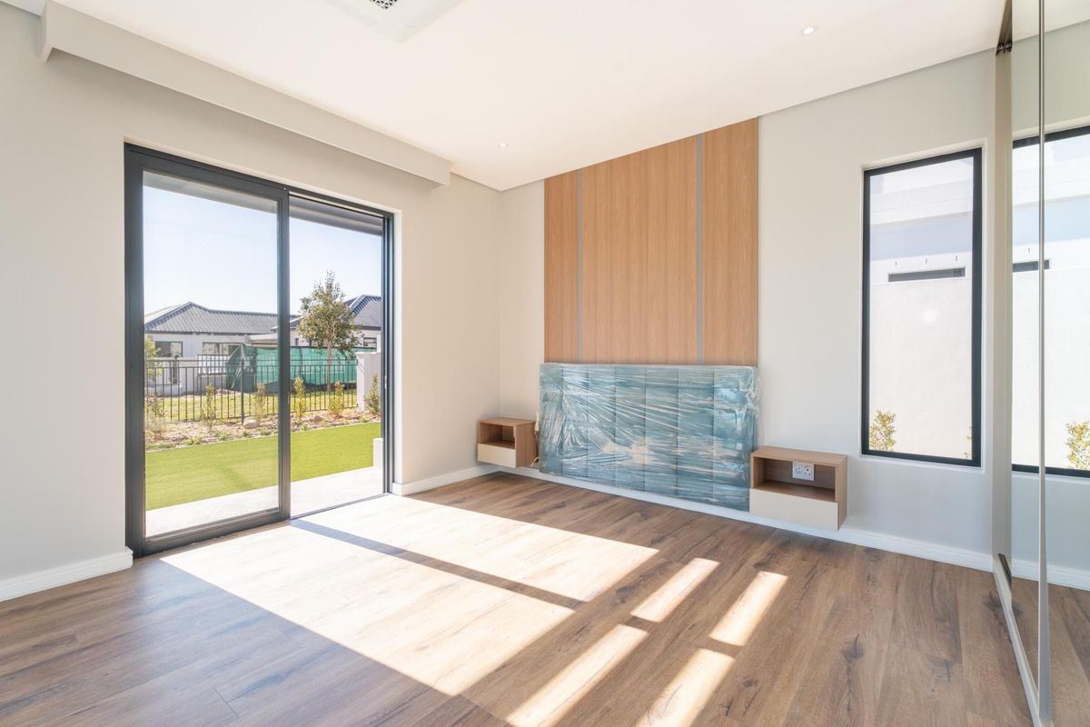A bright, modern bedroom featuring laminate flooring, built-in wall paneling, floating bedside cabinets, and large sliding glass doors leading to the garden.