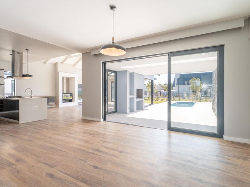 Spacious open-plan living area featuring a modern kitchen, fireplace, and large sliding doors opening to a patio and pool area.