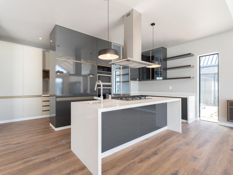 Modern kitchen featuring a central island with stone countertops, high-gloss cabinetry, built-in appliances, and sleek floating shelves, finished with durable laminate flooring.