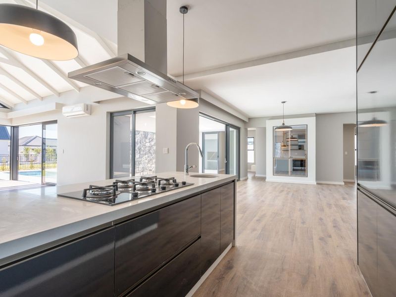 Modern open-plan kitchen and living area featuring a central island with gas hob, sleek cabinetry, and seamless flow to the outdoor patio area.