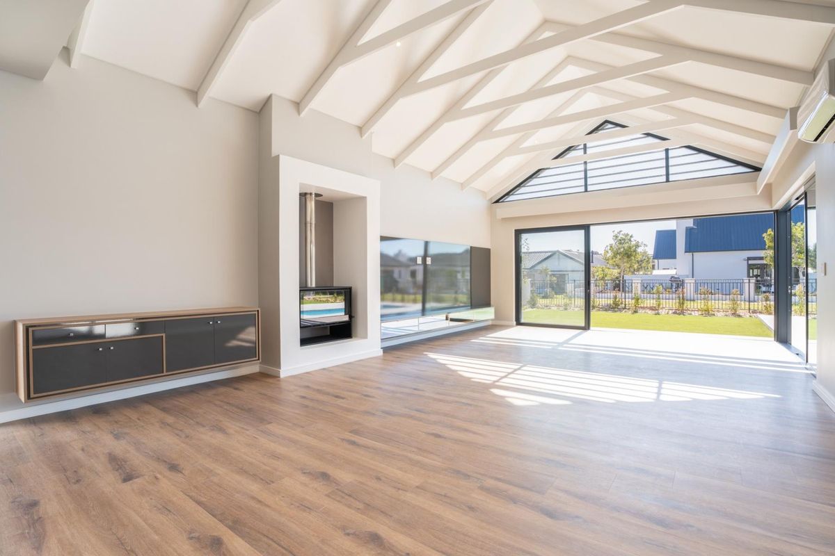 Spacious living area featuring vaulted ceilings with exposed rafters, a modern built-in fireplace, and large sliding glass doors opening to the garden.